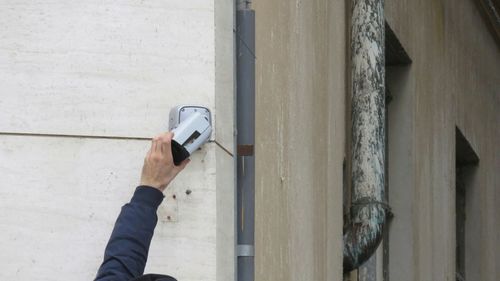 Cropped hand repairing security camera against wall