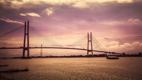 View of suspension bridge over river against cloudy sky