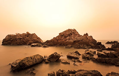 Rocks in sea against clear sky during sunset