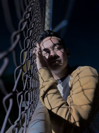 Portrait of young man standing by chainlink fence