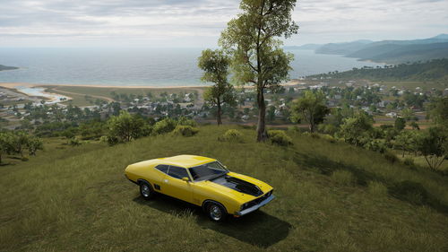 Yellow car on land by sea against sky