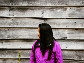 Woman wearing purple jacket standing against wooden wall
