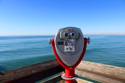 Close-up of coin-operated binoculars by sea against clear sky