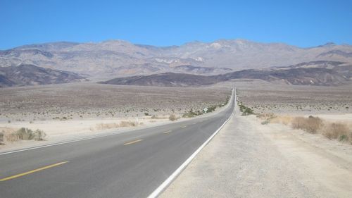 Empty long road leading towards mountain against clear blue sky