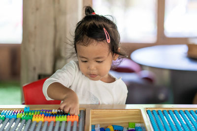 Cute girl playing with toy blocks on table at home