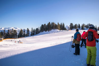 People on snow covered field against clear sky