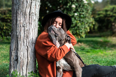 Side view of woman with dog by tree trunk