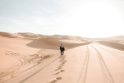 Man on sand dune in desert against sky