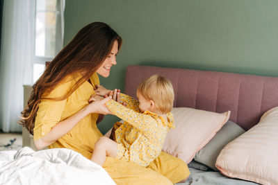 Side view of young woman sitting on bed at home