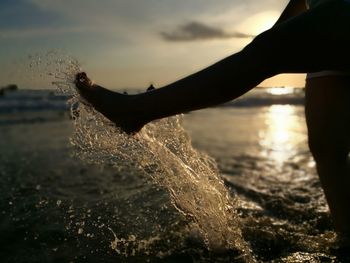 Close-up of leg splashing water at beach against sky