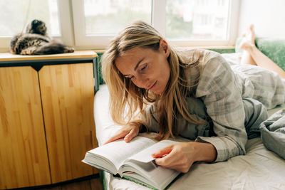 Attractive freckled thirties woman reading a book while lying in bed. person