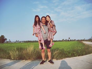 Portrait of smiling father with daughters standing on field against sky