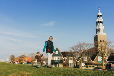 Grandfather and granddaughter walking on field against sky