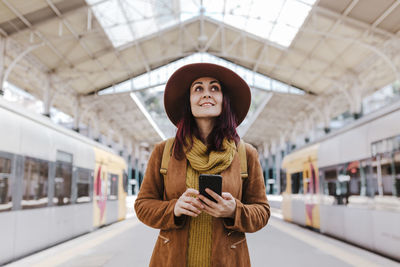 Smiling woman using smart phone while standing at railroad station platform