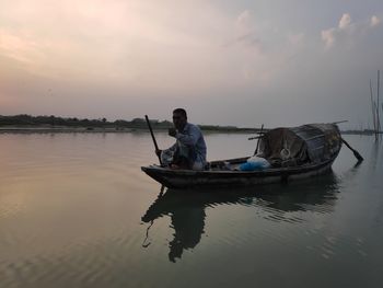 Man on boat in sea against sky during sunset