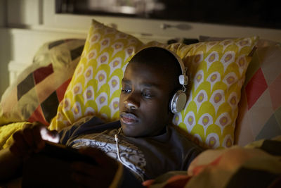 Close-up of boy with headphones using digital tablet while lying on bed at home