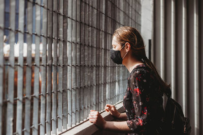 Side view of young woman wearing mask looking through window