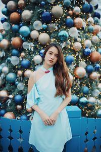 Portrait of smiling young woman standing by christmas tree outdoors