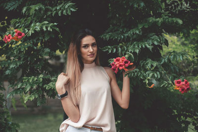 Portrait of beautiful woman standing by flowering plants