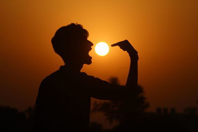 Optical illusion of silhouette man eating sun in sky during sunset