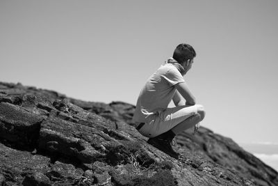 Side view of young woman on rock against sky