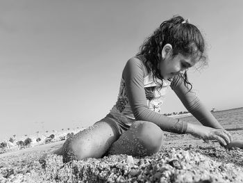 Girl sitting on beach against clear sky