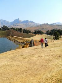 Rear view of couple walking on field by lake against mountains