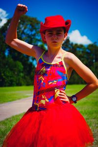 Portrait of teenage girl wearing dress and hat standing against trees in park