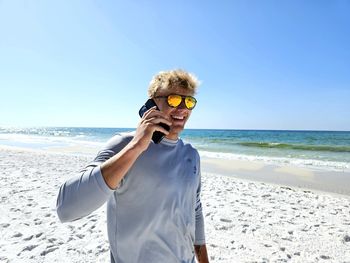 Happy millennial talking on cellphone on the beach.