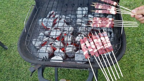 Cropped hand of person holding meat skewers over barbecue at back yard