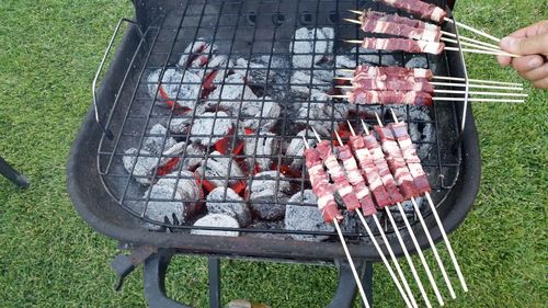 Cropped hand of person holding meat skewers over barbecue at back yard