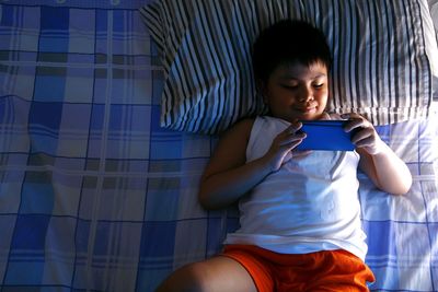 High angle view of boy using smart phone while lying down on bed at home