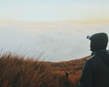 Rear view of man hiking on grassy field against sky