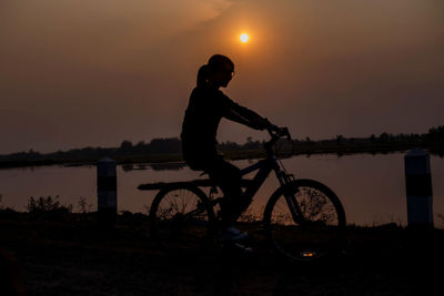 Silhouette man riding bicycle against sky during sunset