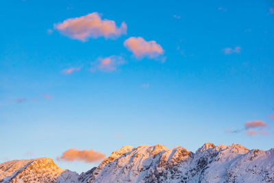 Low angle view of snowcapped mountains against blue sky