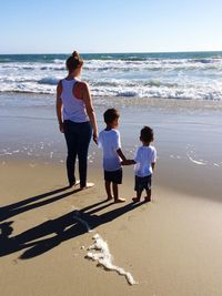 Rear view of mother with son standing at shore against clear sky