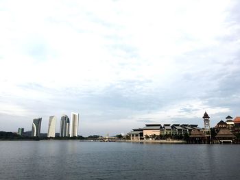 Buildings at waterfront against cloudy sky