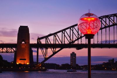 Illuminated bridge over river at sunset