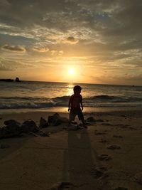 Silhouette boy at beach against sky during sunset