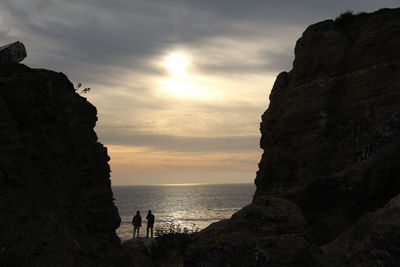 Silhouette cliff by sea against sky during sunset