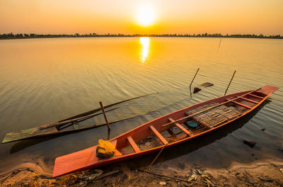 Boat moored in lake against sky during sunset