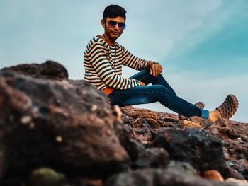 Young man wearing sunglasses on rock against sky