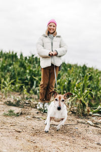 Cute teenage girl walking her dog jack russell terrier on a leash in a field against a background