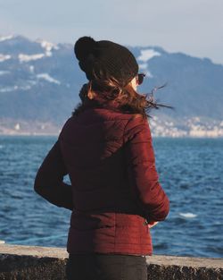 Young woman standing by sea against mountain during winter