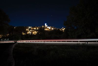 Light trails on illuminated city against sky at night