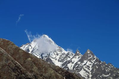 Low angle view of snowcapped mountains against clear blue sky