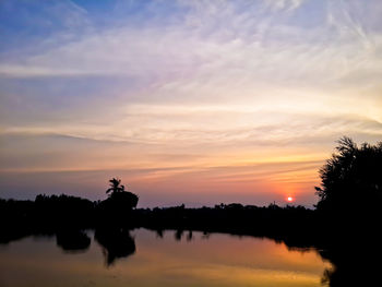 Silhouette trees by lake against sky during sunset