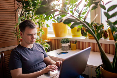 Man works with laptop remotely from home. distant work place with green-nature inspired home office