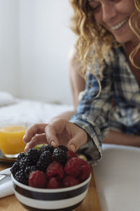 Close up of woman's hand taking a berry of a breakfast tray on the bed