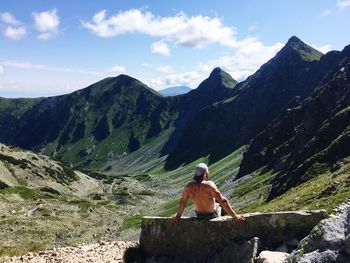 Rear view of man sitting on mountain against sky